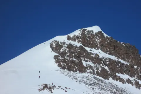 Grupa alpinistów wspina się na najwyższy szczyt Grenlandii, pokonując śnieżne zbocza i skaliste fragmenty.
