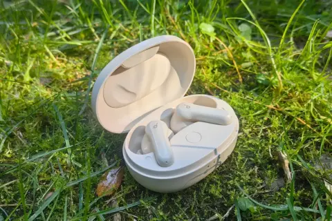 Soundcore P2 Mini Test: Kompakte weiße Ohrhörer in ihrer Ladeschale, umgeben von grünem Gras und Morgentau.