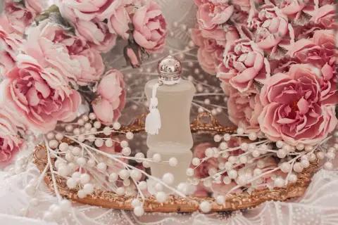 Flakonik Valaya Parfums de Marly otoczony różowymi różami i perłami, na złotym lustrzanym tacy.