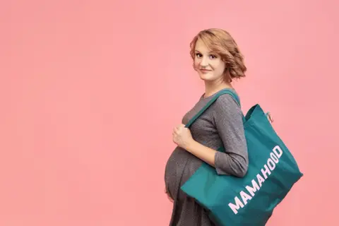 Przyszła mama z torbą "Mamahood" na ramieniu, gotowa do porodu.