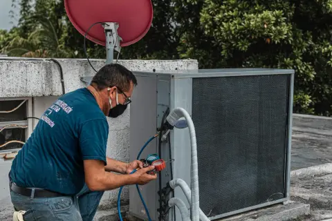 Technik sprawdza czujnik ciśnienia klimatyzacji, podłączając manometr do jednostki zewnętrznej.