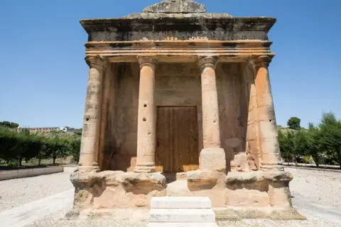 El mausoleo de Fabara, con sus columnas y puerta de madera, se alza imponente bajo un cielo azul.