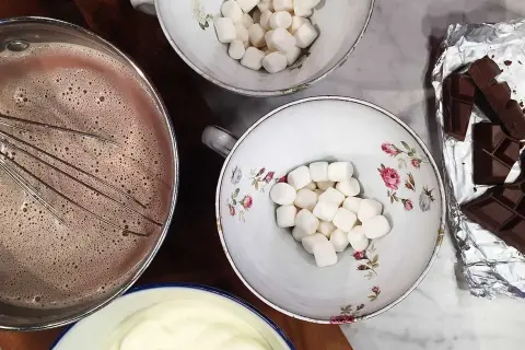 Förberedelser för en mysig stund med varm choklad. Vispad choklad i kastrull, marshmallows i skålar och chokladkakor redo att smältas.