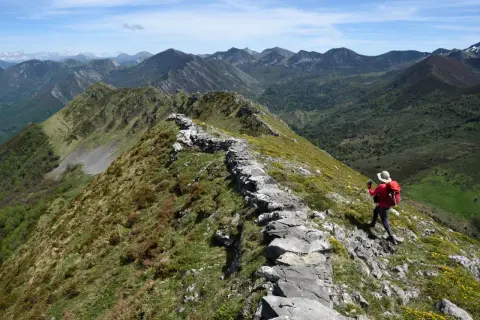 Senderista en cresta rocosa, disfrutando de vistas panorámicas de montañas verdes. Un ejemplo de las mejores rutas de senderismo en España.