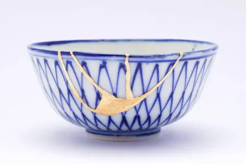 Cuenco de cerámica azul y blanco reparado con la técnica japonesa de kintsugi, resaltando las grietas con oro.