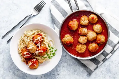 Pulpety w sosie pomidorowym na talerzu ze spaghetti i w rondelku.