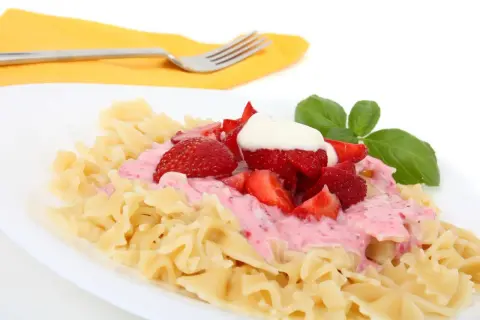 Makaron z truskawkami i kremowym sosem, udekorowany listkiem bazylii. Pyszne danie, które zaskoczy smakiem.