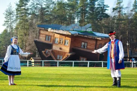 Para z ludźmi w strojach ludowych zaprasza do Domu do Góry Nogami, jednej z głównych atrakcji dla dzieci w Szymbarku.