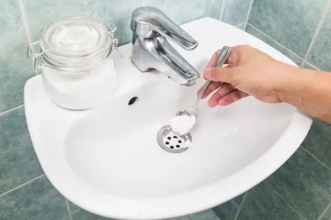 Mano versa bicarbonato nel lavandino per pulire le tubature.