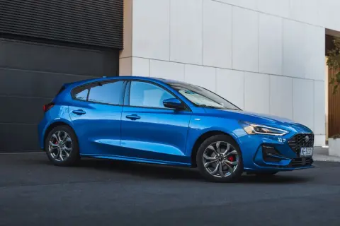 Błękitny hatchback Ford Focus stoi przed nowoczesnym budynkiem.