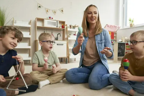 Nauczycielka prowadzi zajęcia z dziećmi, które grają na instrumentach. Wszyscy bawią się, używając zabawki muzyczne dla dzieci.