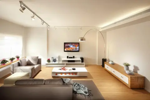 Iluminar un salón moderno con focos dirigibles y una lámpara de arco. Sofás grises, mesa de centro blanca y mueble de TV.