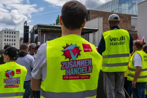 Menschen in Warnwesten mit der Aufschrift "ZUSAMMEN HANDELN FÜR BESSERE TARIFE!" bei Tarifverhandlungen im Einzelhandel.