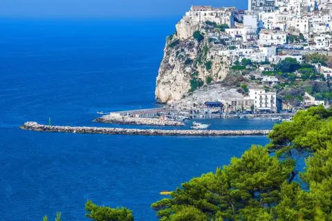 Rodi Garganico, Puglia: case bianche aggrappate alla scogliera, un porto con barche e il mare blu intenso.