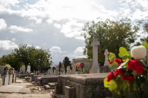 Nagrobek z krzyżami i kwiatami na tle pochmurnego nieba.
