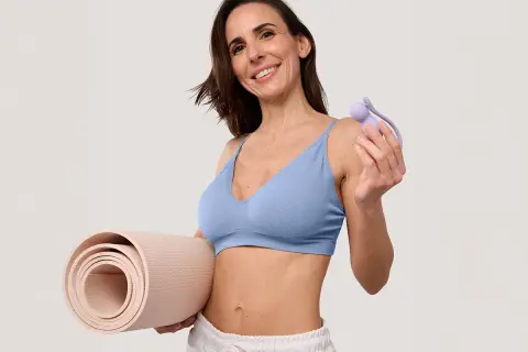 Une femme souriante tient un tapis de yoga et un accessoire pour la musculation du périnée, suggérant quels sont les sports favorables à la musculation du périnée.