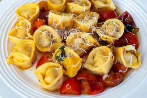 Talerz pełen tortellini z pomidorkami koktajlowymi i startym parmezanem.