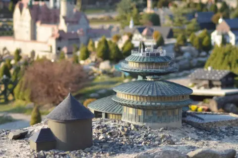 Miniaturowe budowle, w tym okrągły budynek z kopułą i wielopoziomowa konstrukcja, tworzą krajobraz jednego z parków miniatur w Polsce.