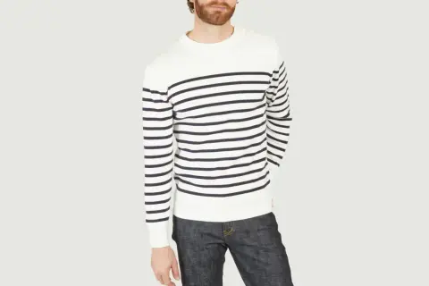 Un homme porte un pull marinière marin à rayures bleues et blanches, avec un jean brut.