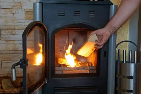 Ein Mann legt Holz in einen brennenden Kamin. Ab wann brennt Holz? Sobald es trocken ist und Zündmaterial vorhanden ist.