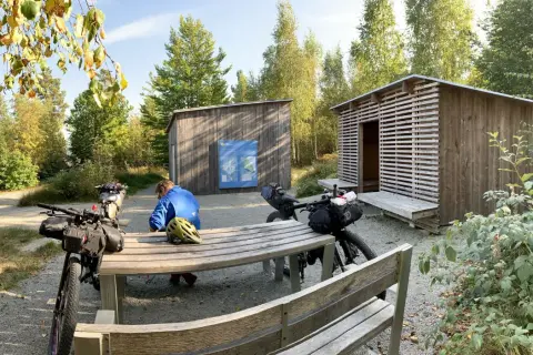 Cykelturist vilar vid rastplats i Åsnen nationalpark. Två packade cyklar står vid ett bord och bänkar.