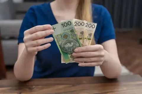 Ręce trzymają banknoty 100 i 200 zł. To wsparcie, które może pomóc w pokryciu kosztów związanych z opieką nad dzieckiem, jak zasiłek rodzicielski.