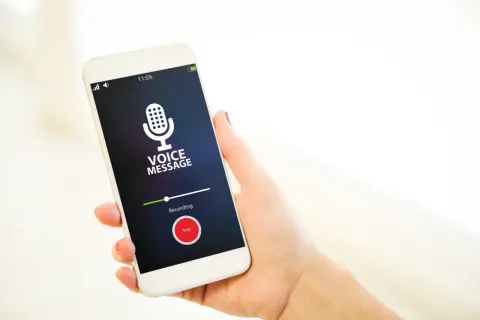 Dłoń trzyma smartfon z ekranem pokazującym interfejs nagrywania wiadomości głosowej. Widoczny jest symbol mikrofonu i przycisk "Stop". To prosty sposób, jak włączyć dyktafon w telefonie.