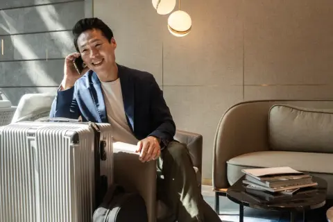 Mann telefoniert in der **Priority Pass Lounge** neben seinem silbernen Koffer. Entspannt wartet er auf seinen Flug.