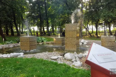 Nowoczesne fontanny w kształcie kostek w parku, otoczone kamieniami i zielenią.