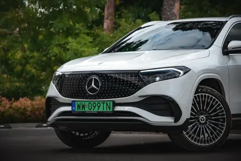 Biały Mercedes EQA z zieloną tablicą rejestracyjną WW 099TN na tle zieleni.