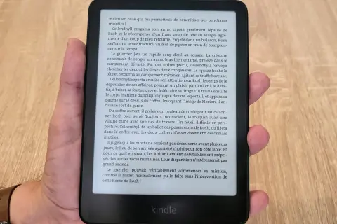 Main tenant un appareil Kindle format e-reader, affichant un texte en français sur fond noir.