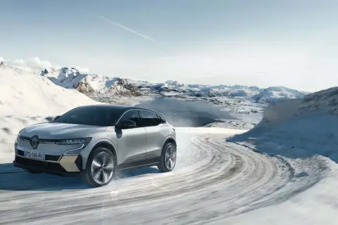 Voiture électrique avec pompe à chaleur traversant un paysage hivernal enneigé, montagnes et lac gelé en arrière-plan.
