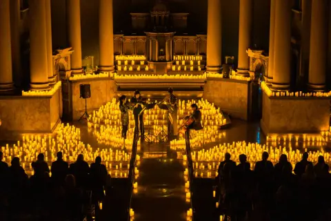 Un concierto de música clásica bajo miles de velas en Pamplona. La luz dorada de la candlelight ilumina a los músicos y al público.