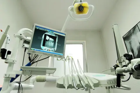 Nowoczesny gabinet stomatologiczny z aparaturą RTG i monitorem wyświetlającym zdjęcie zęba. NZOZ to skrót od Niepubliczny Zakład Opieki Zdrowotnej.