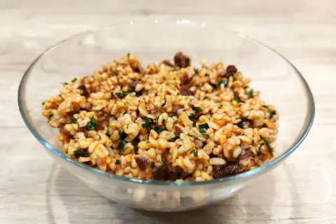 Sałatka z kaszą bulgur i suszonymi pomidorami, pełna smaku i ziół, w szklanej misce.