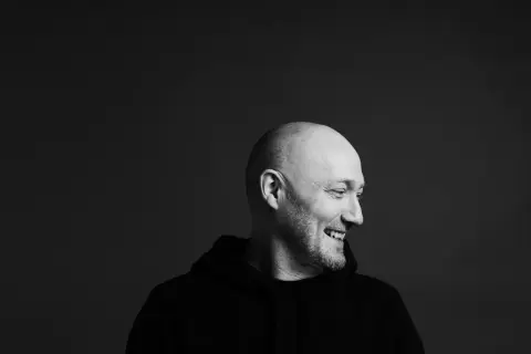 Uśmiechnięty Paul Kalkbrenner w czarnej bluzie, gotowy na koncert w Warszawie.