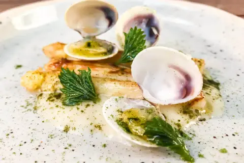 Delizioso piatto con pesce bianco, gamberi e **lupini di mare** in una salsa cremosa, guarnito con erbe fresche.