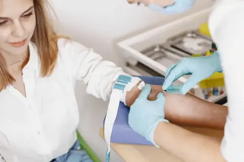 Pobieranie krwi do badań. Kobieta w białej koszuli spokojnie czeka na wynik. Alt co to za badanie?