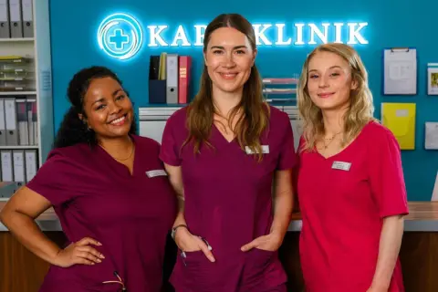 Drei Krankenschwestern lächeln vor dem Schild "Klinik". Staffel 12 von Bettys Diagnose verspricht spannende Fälle.