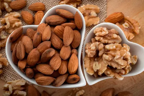 Deux bols en forme de cœur remplis d'amandes et de noix. Une belle présentation de ces oléagineux, parfaits pour une liste d'en-cas sains.