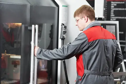Ein Zerspanungsmechaniker öffnet die Tür einer CNC-Maschine. Er erkundet zerspanungsmechaniker weiterbildungsmöglichkeiten.