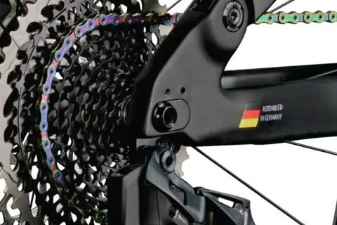 Kolorowy łańcuch rowerowy oplata kasetę zębatek. Widać ramę z napisem "ASSEMBLED IN GERMANY" i flagą. Gwint trójkątny jest kluczowy dla połączeń.