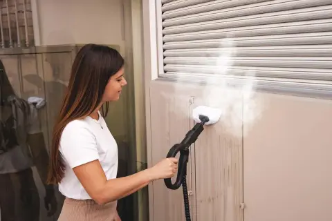 Donna pulisce le tapparelle con un pulitore a vapore, rimuovendo lo sporco in modo efficace.