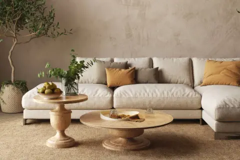 Accogliente salotto con divano chiaro, cuscini ocra e verdi, tavolini in legno e piante. Un'atmosfera rilassante con salotto colori caldi.