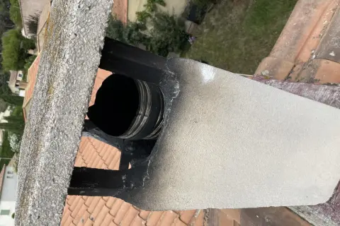 Détail d'un conduit de cheminée en métal noir, visiblement endommagé et encrassé, suggérant la nécessité de comment condamner un conduit de cheminée pour des raisons de sécurité.