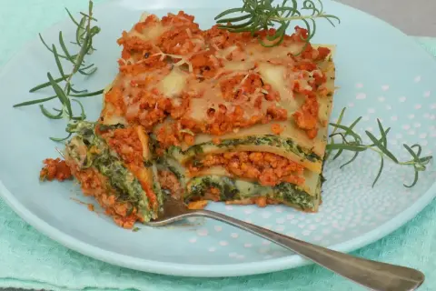Pyszny przepis na lasagne z mięsem mielonym i szpinakiem, podana na talerzu z gałązkami rozmarynu.