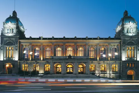 Prachtvolle alte Stadthalle im Abendlicht, beleuchtete Fenster und Türme, Lichterspuren auf der Straße.
