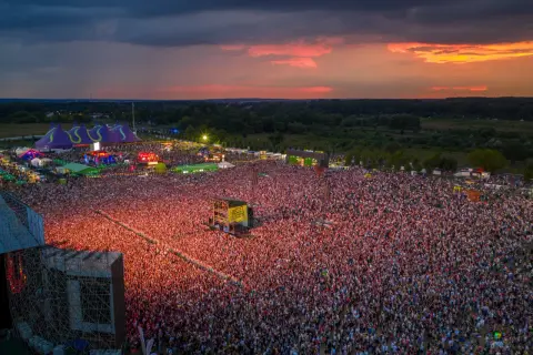 Widok z lotu ptaka na festiwal muzyczny z tłumem ludzi i sceną podczas zachodu słońca.