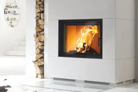 Moderner Kamin mit brennendem Feuer. Holzstapel daneben. Unterschied zwischen Zeitbrand und Dauerbrand ist hier nicht ersichtlich.