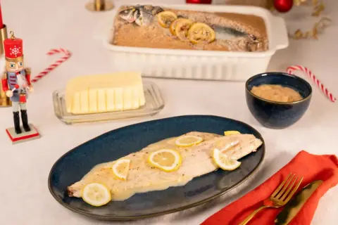 Un bar en croûte de sel, tel que préparé par Julie, est servi avec des rondelles de citron. Un beurre crémeux et une sauce à la moutarde complètent ce plat festif.